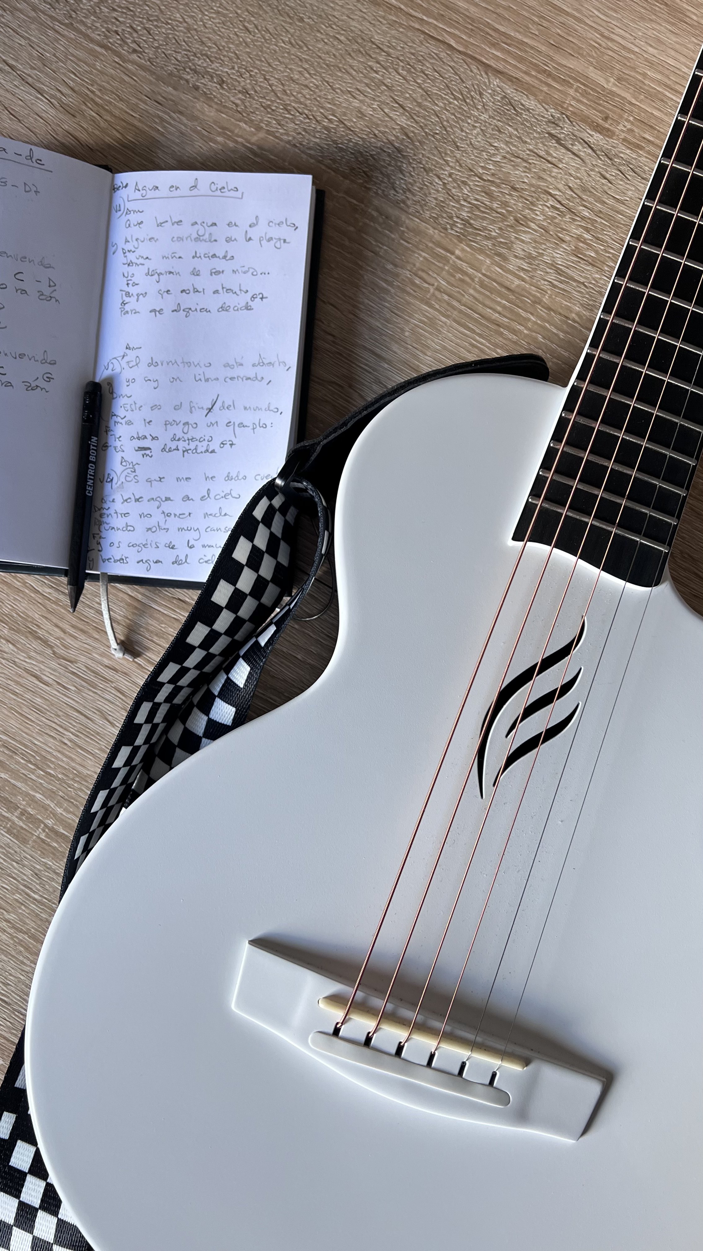 Cuaderno abierto con la letra de una canción escrita a mano, junto a una guitarra